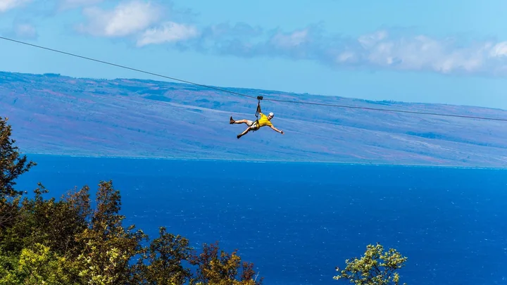 Ein Teilnehmer auf einer langen Zipline hoch über West Maui, dahinter das Meer